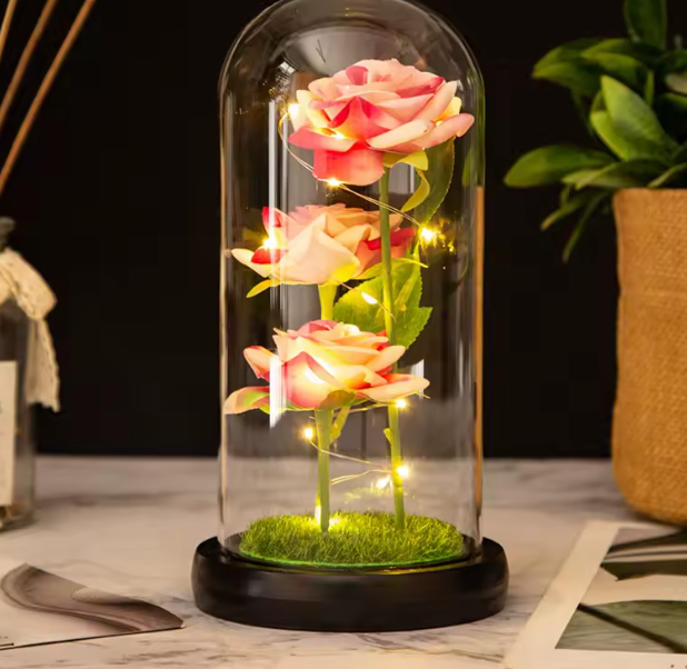 Decorative glass dome with glowing pink roses on a wooden surface.