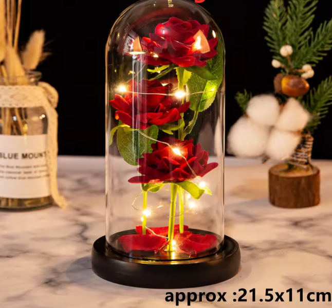 Decorative glass dome with red roses and fairy lights on a marble surface.
