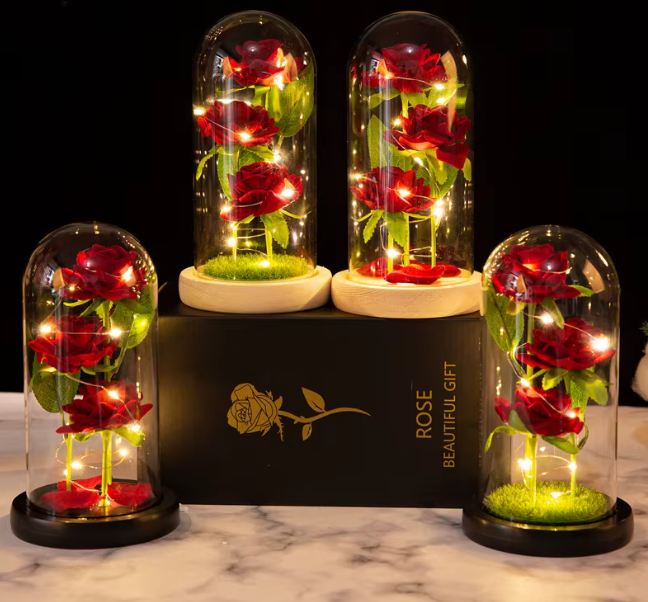 Decorative display of red roses under glass domes with a black box labeled 'Rose Beautiful Gift' on a marble surface.