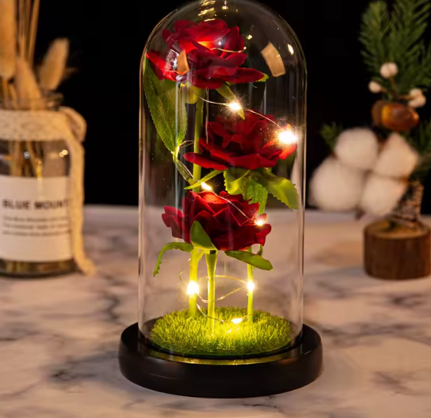 Decorative setup with red roses under a glass dome on a marble surface.