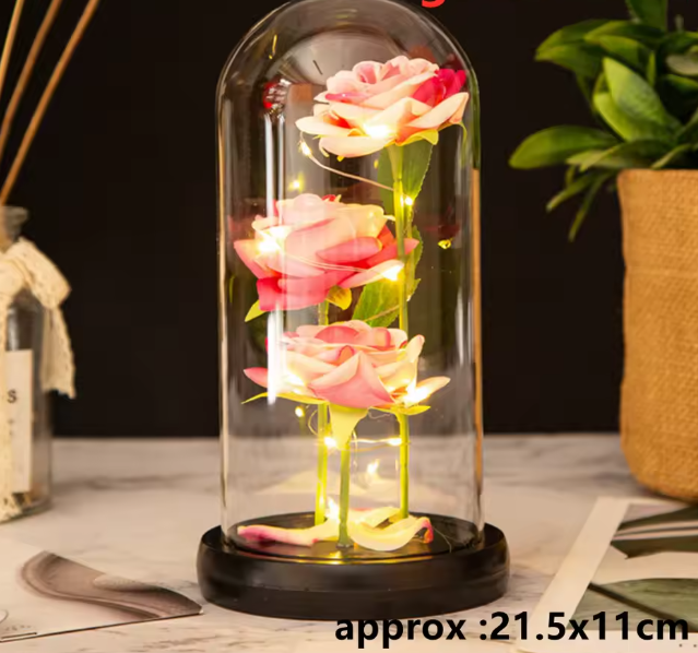 Decorative glass dome with LED lights and pink roses on a wooden surface.